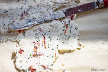 Frischkäse-Kräutercreme wird auf dem ausgerollten Blätterteig verstrichen