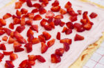 Joghurt-Sahnemischung und kleingeschnittene Erdbeeren auf dem Teig verteilt